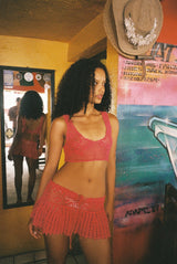 Woman in a red crochet dress standing on a colorful floor with posters in the background