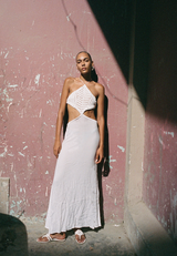 Woman in a white dress standing against a textured wall.